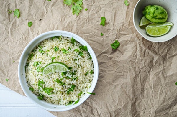 An overhead view of cilantro lime rice in a dish on top of a paper covered table. A small bowl of limes to the right.