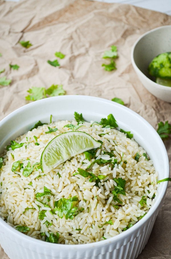 A dish full of cilantro lime rice on a brown paper covered table. Garnished with a lime wedge.